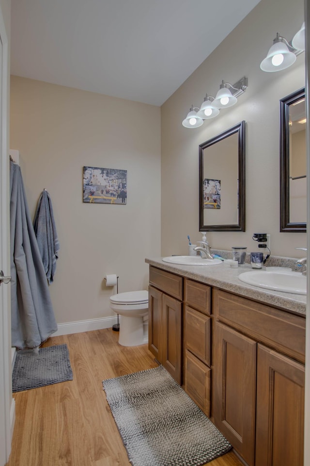 bathroom featuring double vanity, wood finished floors, a sink, and toilet