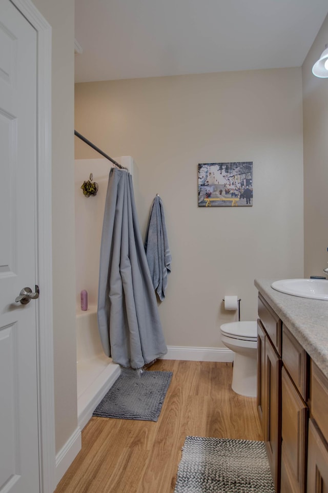 bathroom with curtained shower, toilet, vanity, wood finished floors, and baseboards