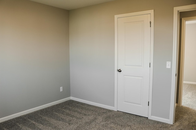 spare room with baseboards and dark colored carpet