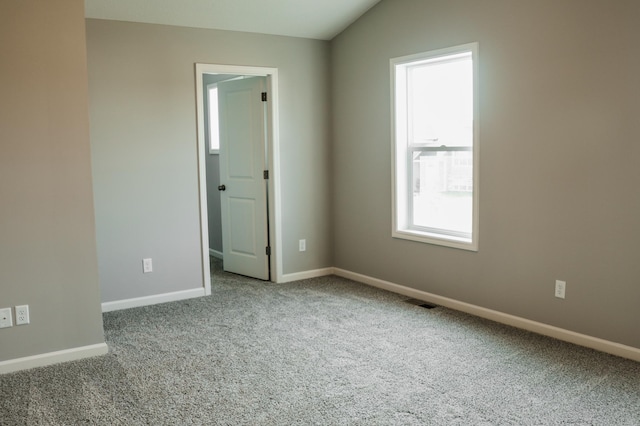 carpeted empty room featuring baseboards and vaulted ceiling