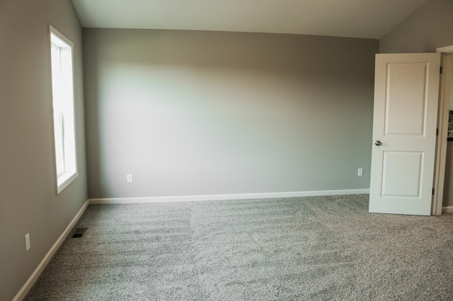 carpeted empty room with visible vents, baseboards, and lofted ceiling