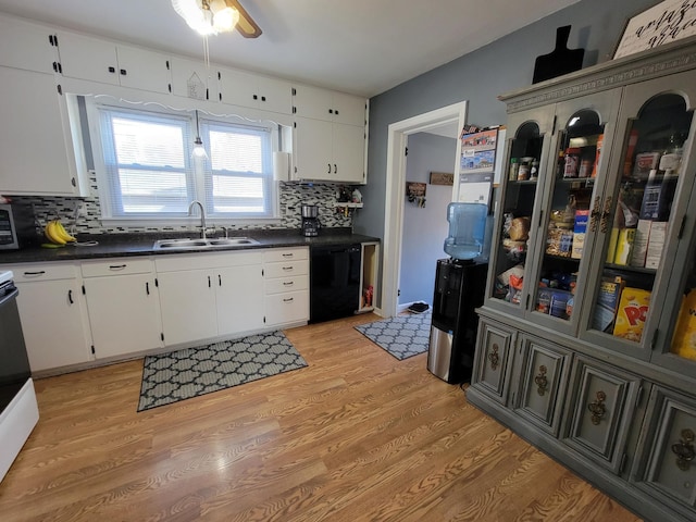 kitchen featuring dark countertops, dishwasher, light wood-style flooring, white cabinets, and a sink