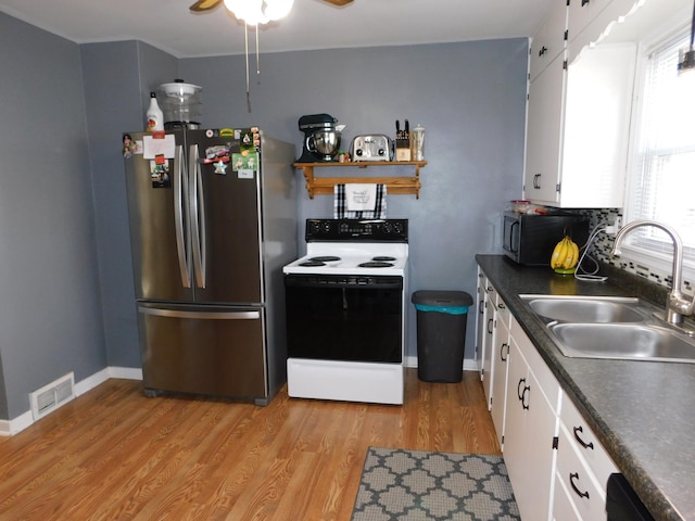 kitchen with light wood-type flooring, a sink, range with electric stovetop, dark countertops, and freestanding refrigerator