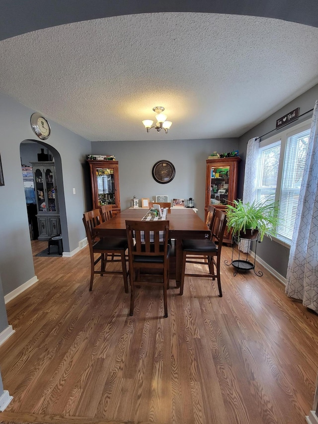 dining room with arched walkways, a textured ceiling, baseboards, and wood finished floors