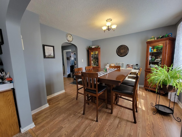 dining space with baseboards, arched walkways, light wood finished floors, and a textured ceiling