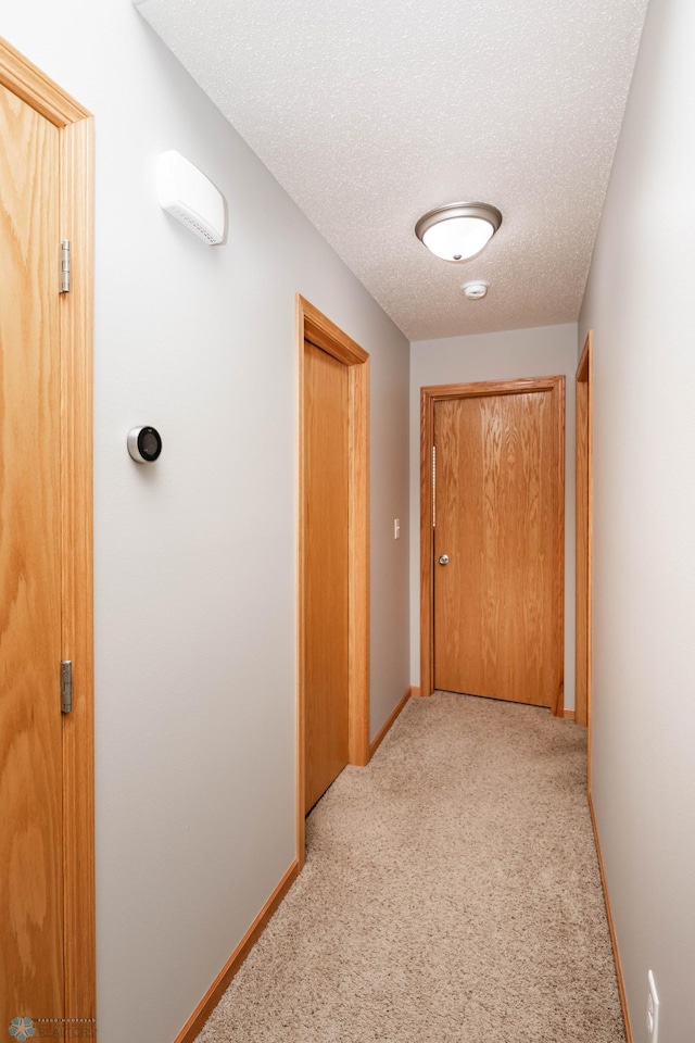 corridor featuring baseboards, light carpet, and a textured ceiling