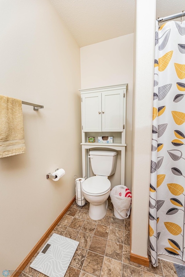 bathroom featuring stone finish floor, toilet, a shower with shower curtain, and baseboards