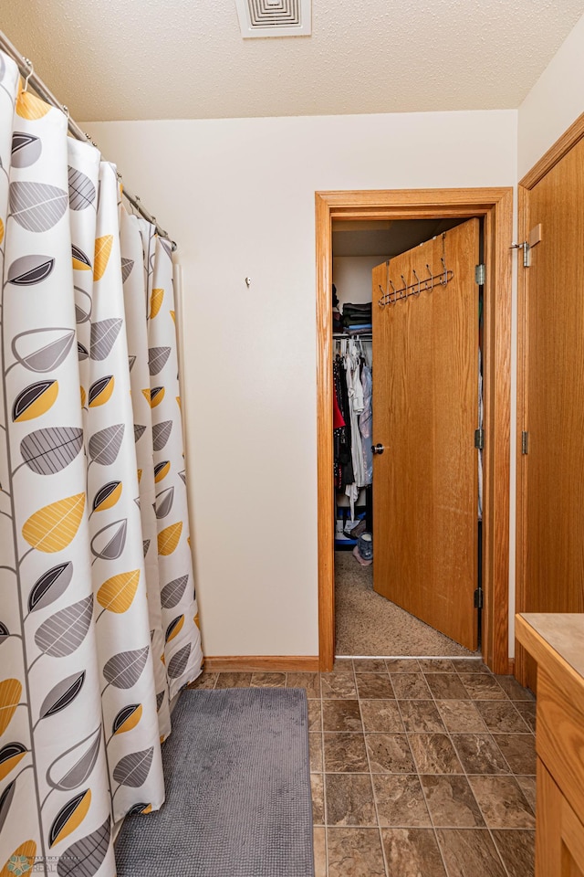 interior space with a shower with shower curtain, visible vents, stone finish floor, a textured ceiling, and a walk in closet