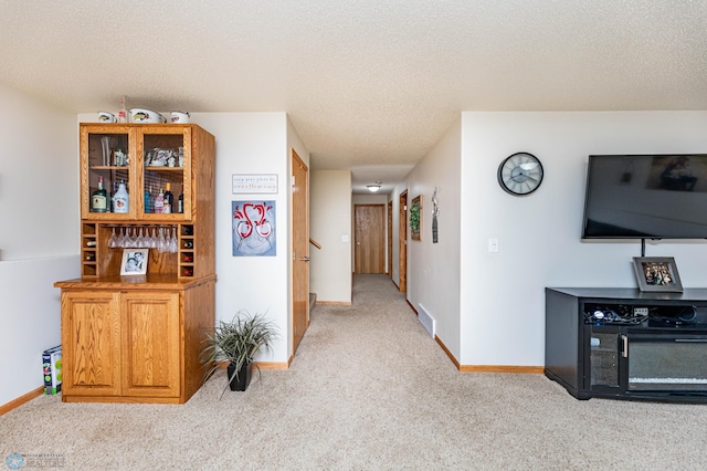 hallway featuring visible vents, a textured ceiling, baseboards, and carpet floors