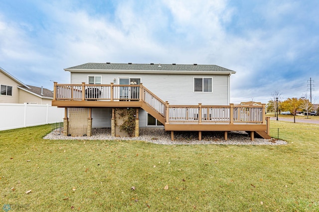 rear view of house featuring a wooden deck, a yard, and fence