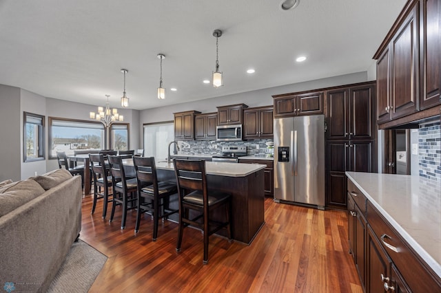 kitchen with wood finished floors, an inviting chandelier, stainless steel appliances, dark brown cabinets, and a kitchen breakfast bar