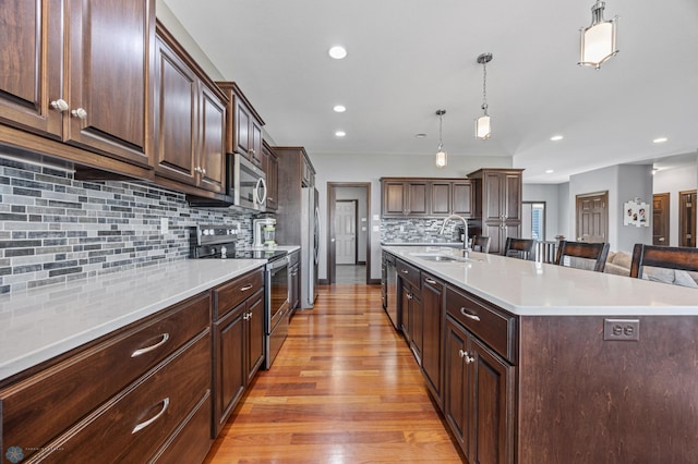 kitchen with a sink, stainless steel appliances, a large island, light countertops, and light wood-style floors