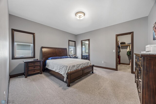 bedroom featuring a walk in closet, baseboards, light colored carpet, and a closet