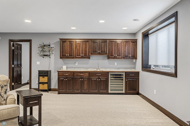 kitchen with wine cooler, dark brown cabinetry, light countertops, and a sink