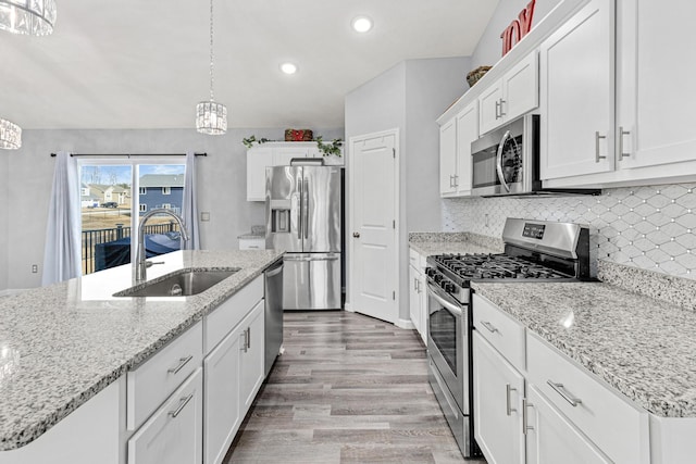 kitchen with appliances with stainless steel finishes, light wood-style flooring, white cabinetry, decorative backsplash, and a sink
