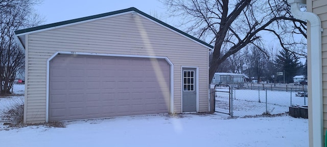 snow covered garage featuring fence and a garage