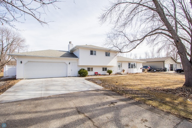 tri-level home with a garage, concrete driveway, and a chimney