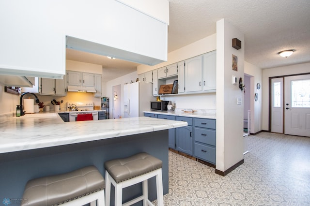 kitchen featuring a peninsula, a sink, light countertops, white fridge with ice dispenser, and stainless steel microwave