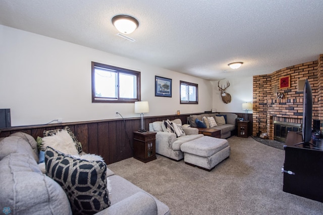 carpeted living area with a textured ceiling, a brick fireplace, wood walls, and wainscoting