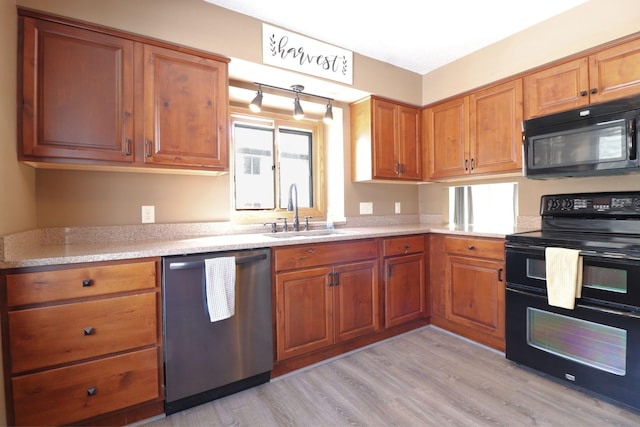 kitchen with light wood-type flooring, brown cabinets, black appliances, a sink, and light countertops