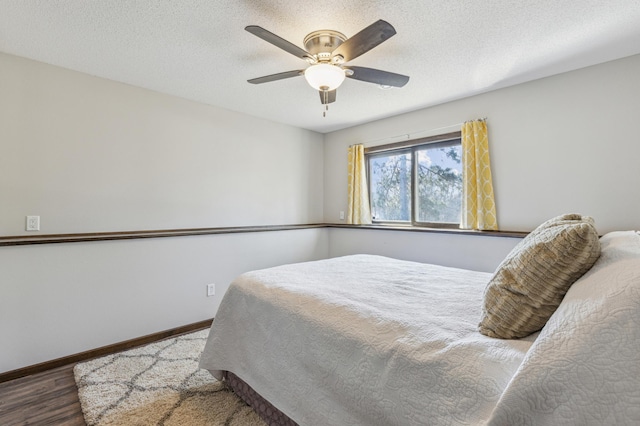 bedroom featuring a ceiling fan, wood finished floors, baseboards, and a textured ceiling