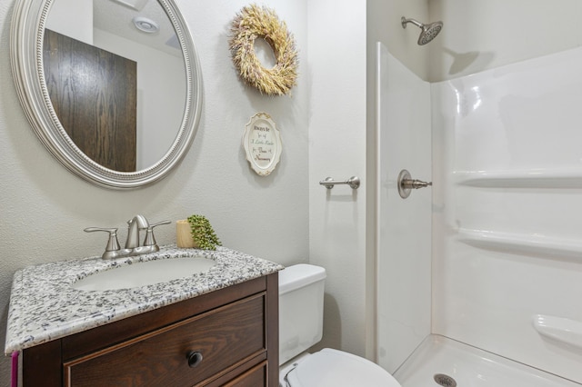 bathroom with toilet, a stall shower, vanity, and a textured wall