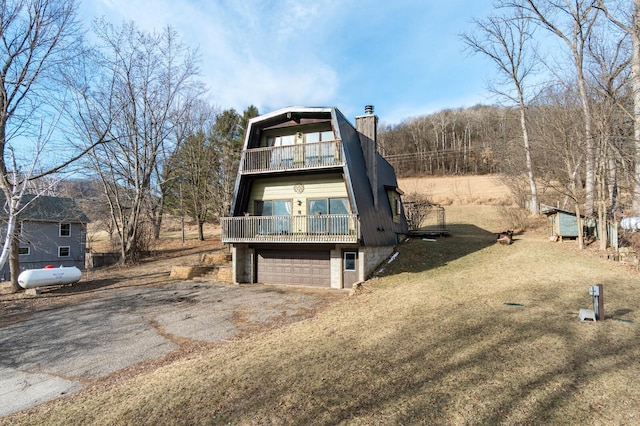 view of front of house with aphalt driveway, a balcony, a garage, and a chimney