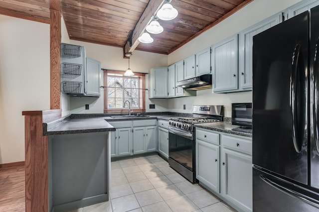 kitchen featuring under cabinet range hood, stainless steel gas range, dark countertops, and freestanding refrigerator