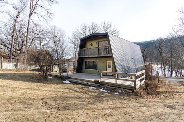 back of property featuring a deck, a balcony, fence, and a gambrel roof