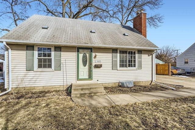 view of front facade featuring a shingled roof, a chimney, and fence