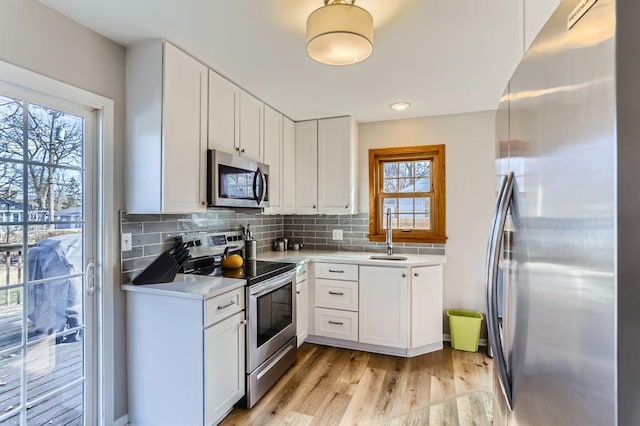 kitchen featuring a sink, appliances with stainless steel finishes, white cabinetry, light wood-type flooring, and backsplash