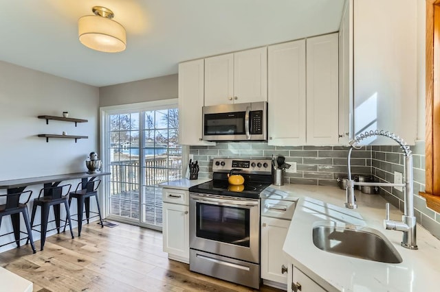 kitchen with a sink, white cabinetry, backsplash, and stainless steel appliances