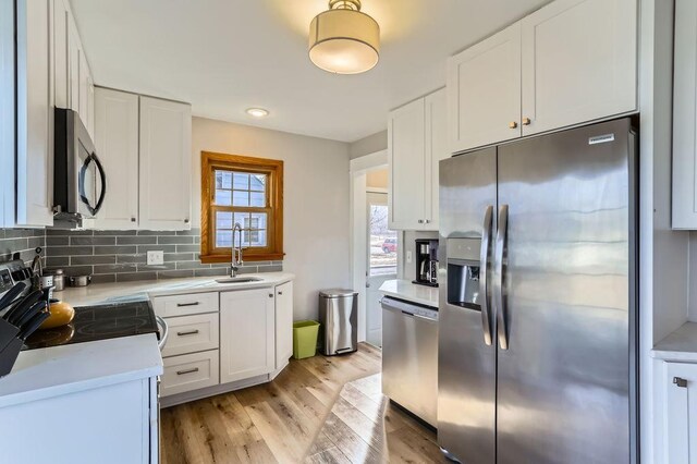 kitchen featuring light wood finished floors, a sink, white cabinets, appliances with stainless steel finishes, and tasteful backsplash