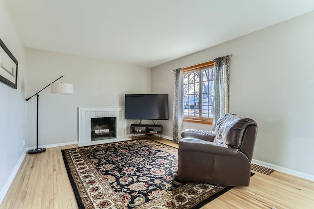 living area featuring visible vents, a brick fireplace, baseboards, and wood finished floors