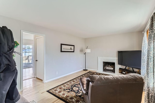 living area featuring light wood-style flooring, a brick fireplace, and baseboards