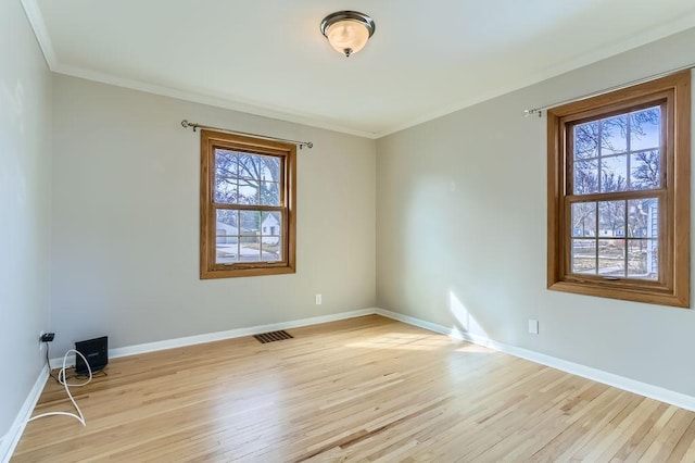 spare room with visible vents, light wood-style flooring, baseboards, and ornamental molding