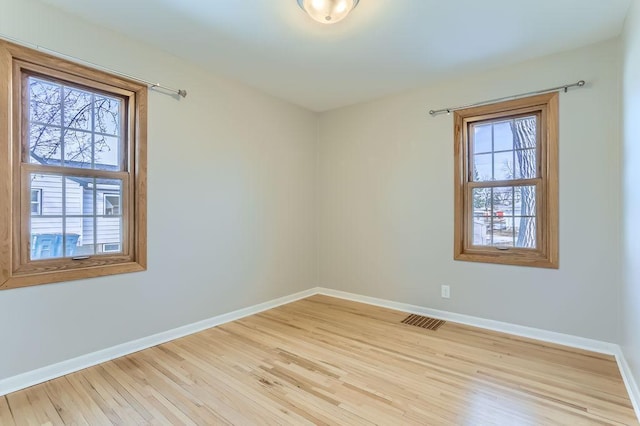 empty room with visible vents, a healthy amount of sunlight, baseboards, and wood finished floors