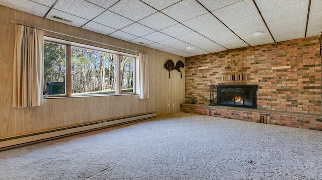 unfurnished living room with baseboard heating, a brick fireplace, wood walls, and carpet flooring