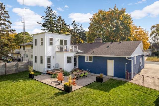 rear view of property with a balcony, fence, a shingled roof, a patio area, and a lawn