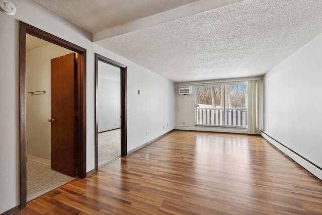 unfurnished room featuring a wall mounted air conditioner, baseboard heating, wood finished floors, and a textured ceiling