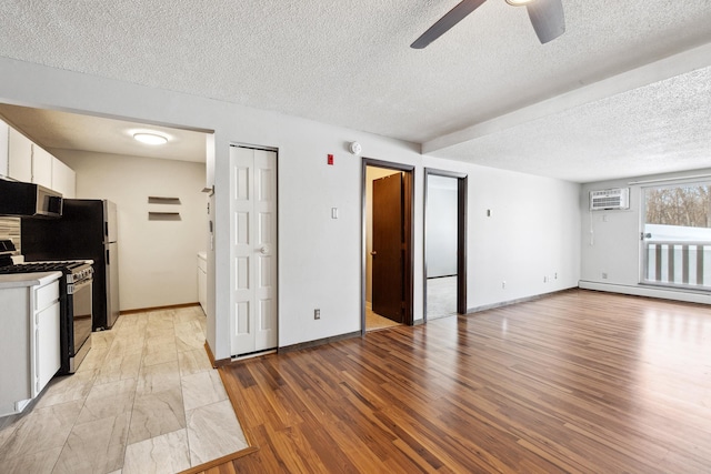 kitchen featuring a wall mounted AC, light wood-style flooring, white cabinets, gas range, and baseboard heating