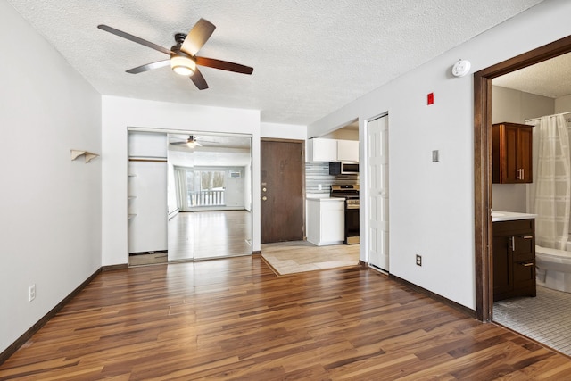 unfurnished living room with ceiling fan, a textured ceiling, baseboards, and wood finished floors