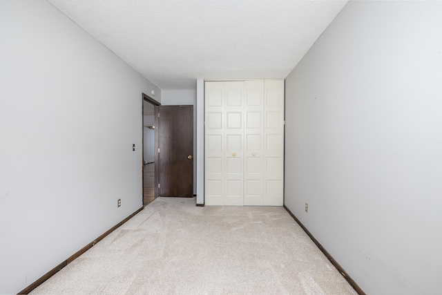 unfurnished bedroom with a closet, light colored carpet, a textured ceiling, and baseboards