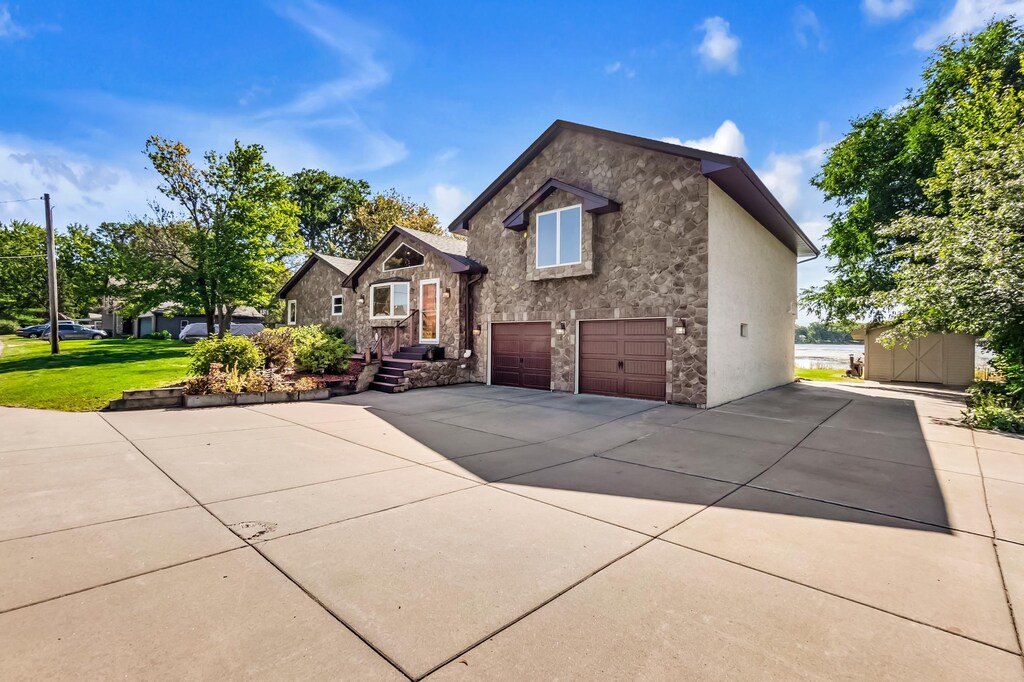 view of front of house with a garage, stone siding, a front yard, and driveway