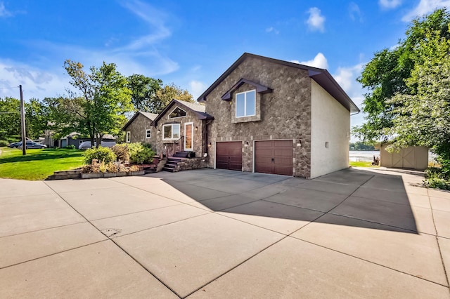 view of front of house with a garage, stone siding, a front yard, and driveway