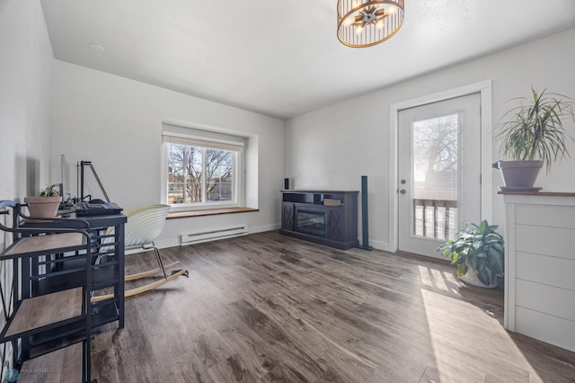 office area with wood finished floors, baseboards, a baseboard radiator, a glass covered fireplace, and a chandelier