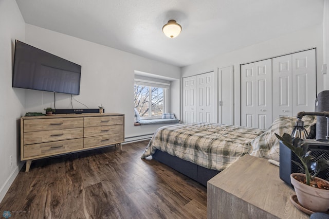 bedroom with dark wood-style floors, two closets, a baseboard heating unit, and baseboards