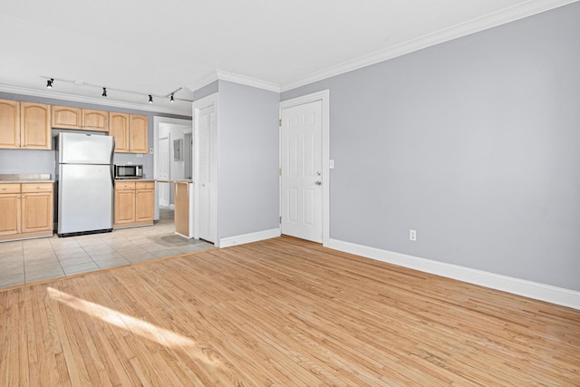 kitchen featuring stainless steel microwave, light countertops, ornamental molding, freestanding refrigerator, and light wood-style floors