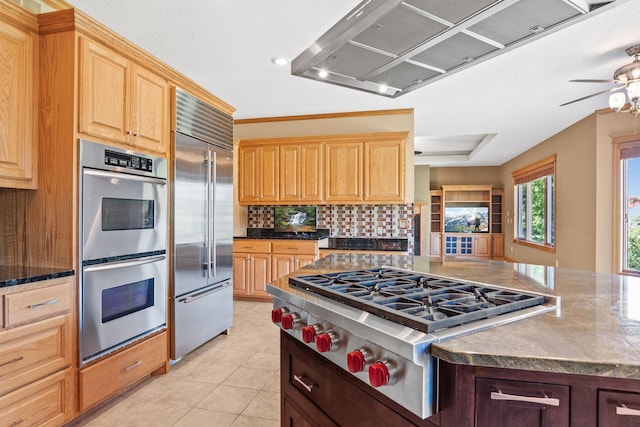 kitchen featuring light tile patterned flooring, ceiling fan, decorative backsplash, stainless steel appliances, and wall chimney range hood