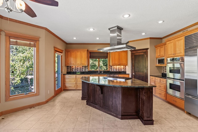 kitchen featuring island exhaust hood, tasteful backsplash, built in appliances, a center island, and baseboards